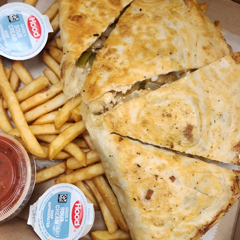 A calzone cut in half, revealing its cheesy filling, served with fries, marinara, and sour cream.