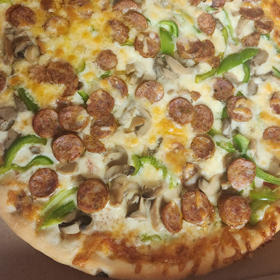 A close-up of a Hudson House of Pizza pizza with sausage, mushrooms, and green peppers.