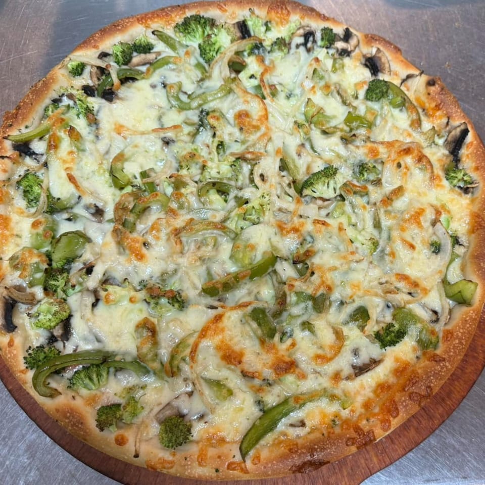 A whole vegetarian pizza with broccoli, green peppers, onions, and mushrooms on a wooden peel.