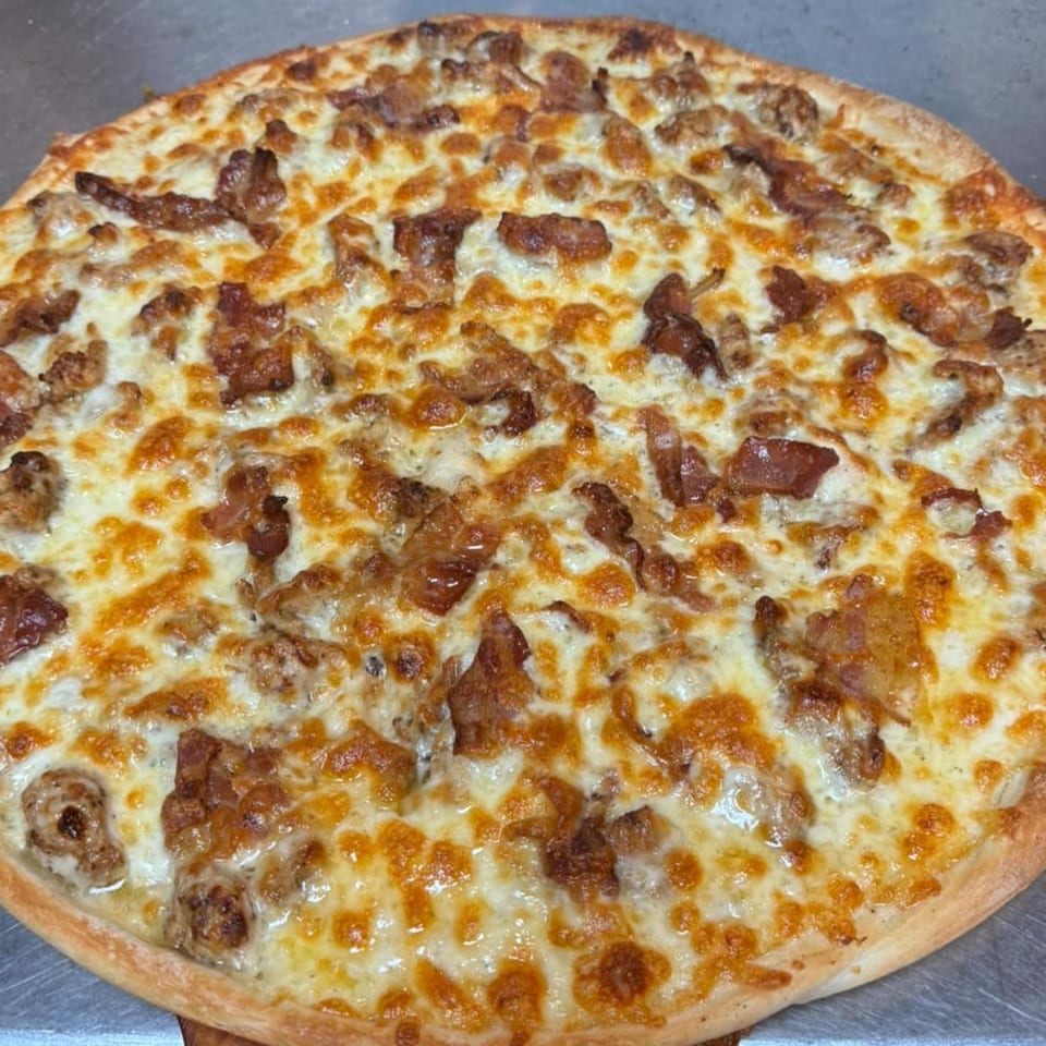 A close-up of a Hudson House of Pizza bacon pizza with melted cheese and a golden crust.